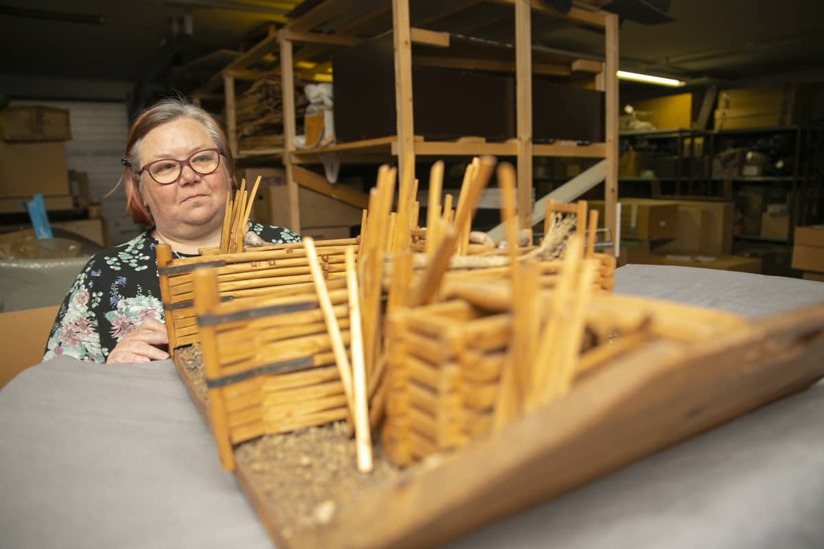 Silmälasipäinen nainen tarkastelee vanhaa ankeriaspadon pienosmallia