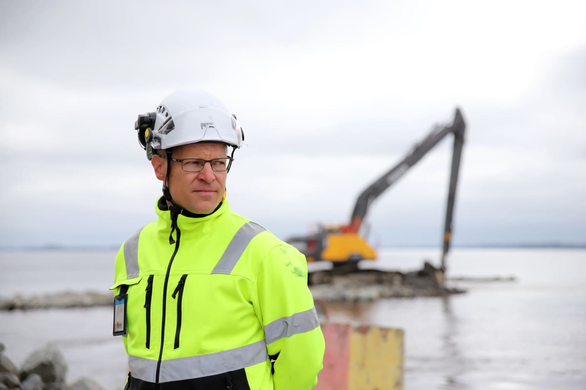 Janne Ikonen Savon Kuljetukselta seuraa lossirannan rakennustöiden etenemistä Liperissä, taustalla kaivinkone.