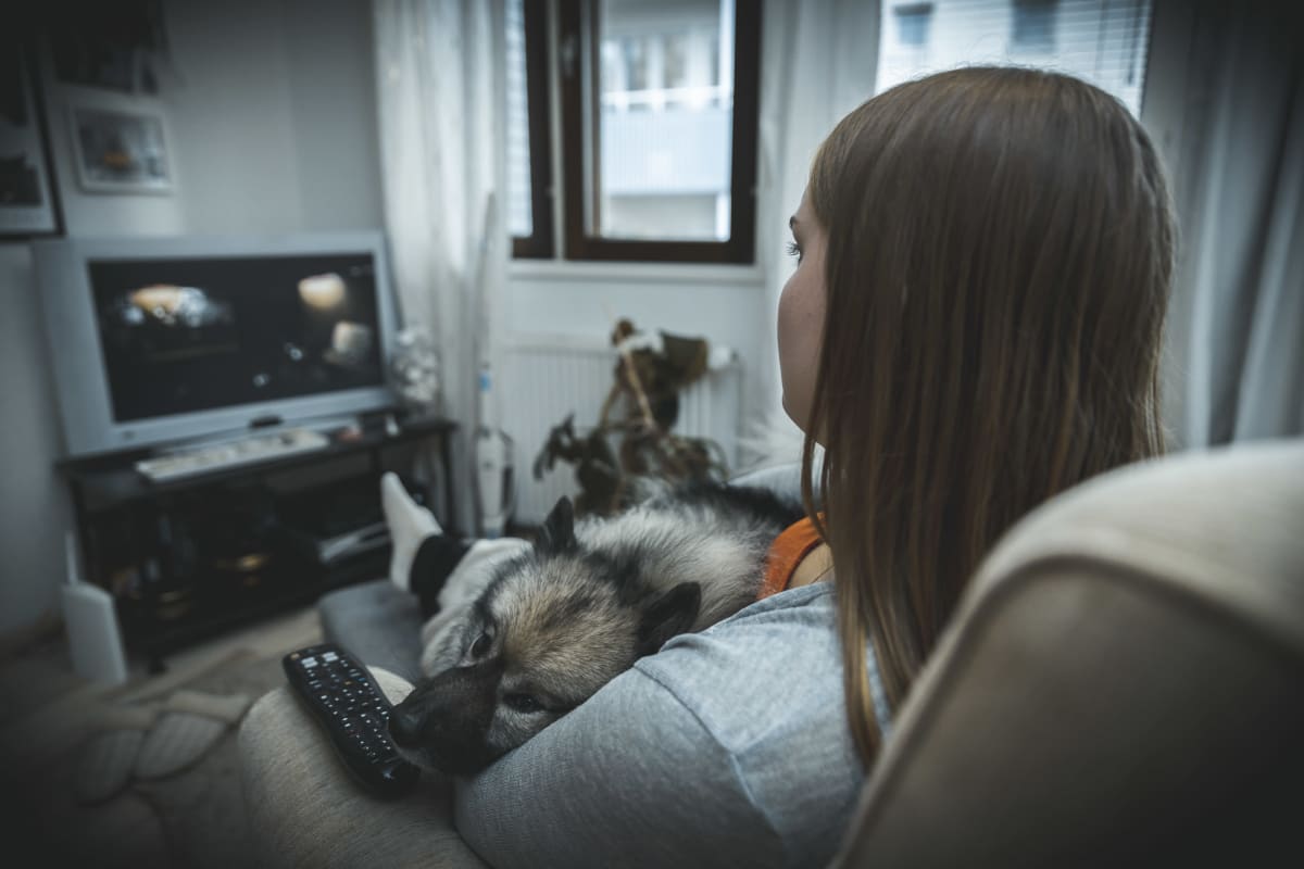 Petra Suonperä koira sylissään katsoo sohvalla kauhuelokuvaa.