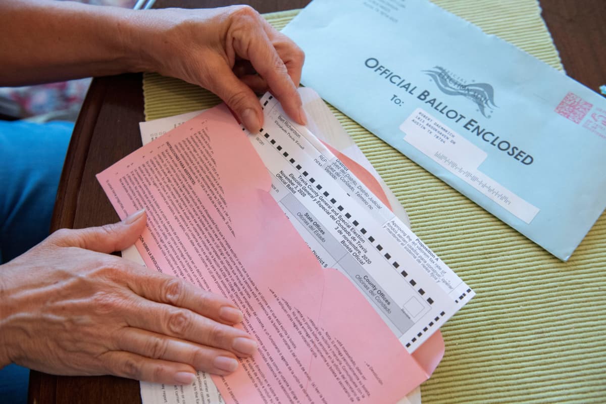 Lähikuvassa nainen sulkee vaalilippua postikuoreen. Kuoressa lukee englanniksi: Official Ballot Enclosed.