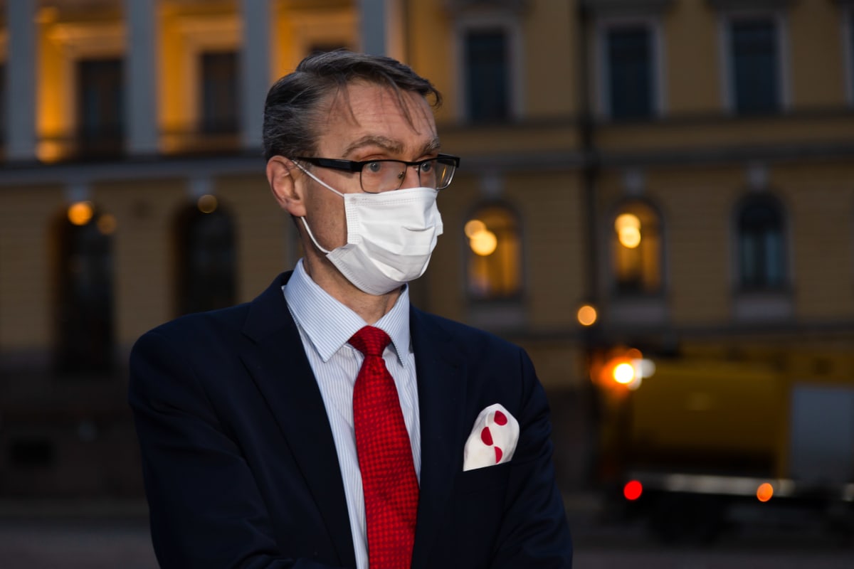 Tuomas Pöysti hämärtyvässä illassa Senaatintorilla. Tuomas on pukeutunut tummansiniseen pukuun. Vaaleansinisen kauluspaudan parina on punainanen kravatti ja rintataskusta pilkistää punaisilla ympyröillä koristeltu valkonen liina. Kasvomaski on käytössä.