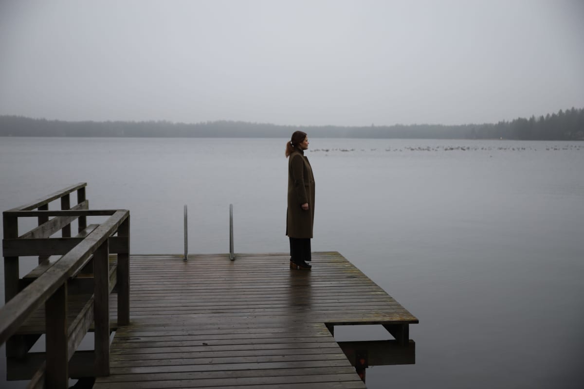 nainen seisoo laiturilla, katselee sumuiselle järvelle