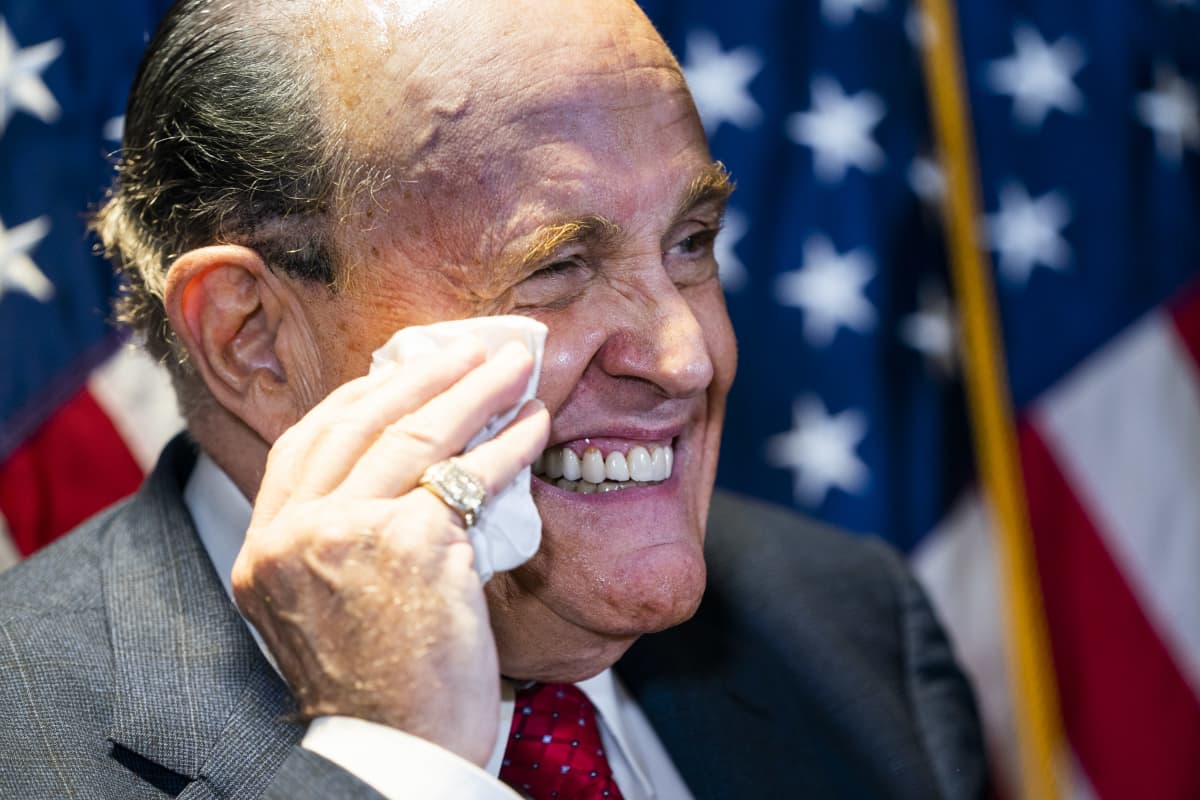 Lähikuvassa hymyilevä Rudy Giuliani pyyhkii nenäliinalla hikeä kasvoiltaan.