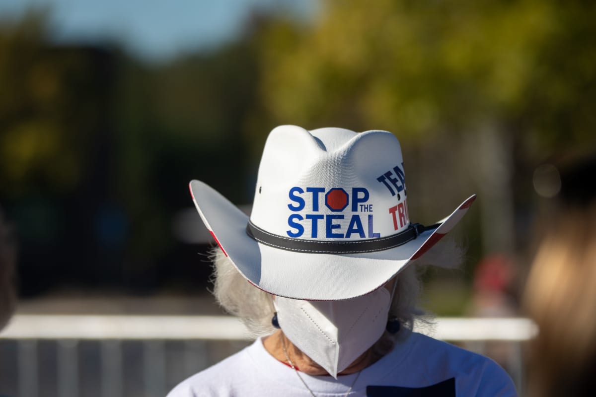 Cowboy hattuinen Trumpia kannattava nainen kasvomaskissa. Valkoisessa hatussa lukee englanniksi: Stop the steal.