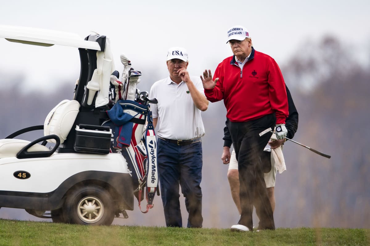 Presidentti Trump tervehtii kuvaajia golfi pelatessaan. Kuvassa vasemmalla Trumpin käytttämä golfauto.