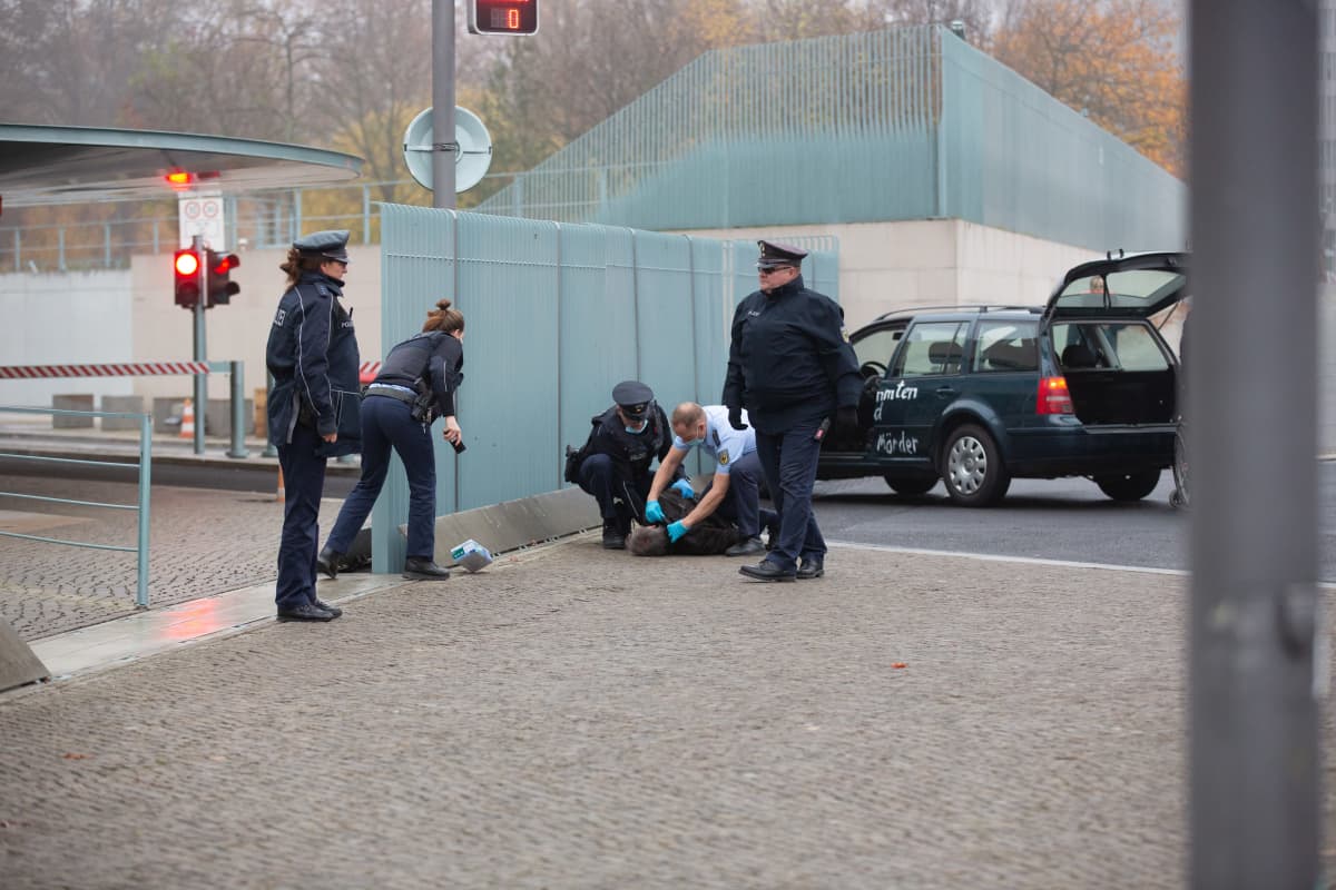 Maassa makaava mies ja poliiseja.