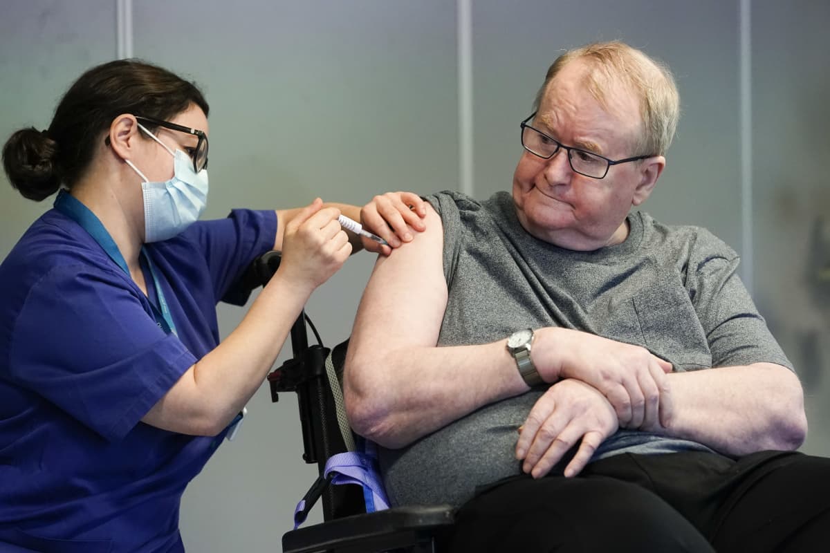 Man på servicehem får vaccin i armen av vårdpersonal med munskydd.