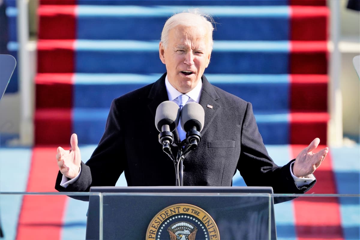 Biden puhuu puhujanpöntön takaa lavalla kongressitalon edustalla. Hän nostaa molempia käsiään.