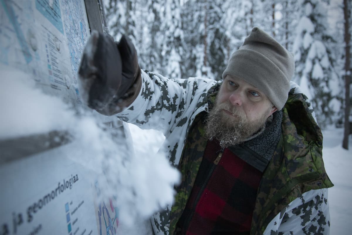 Mikko Kettunen puhdistaa opastekylttiä lumesta.