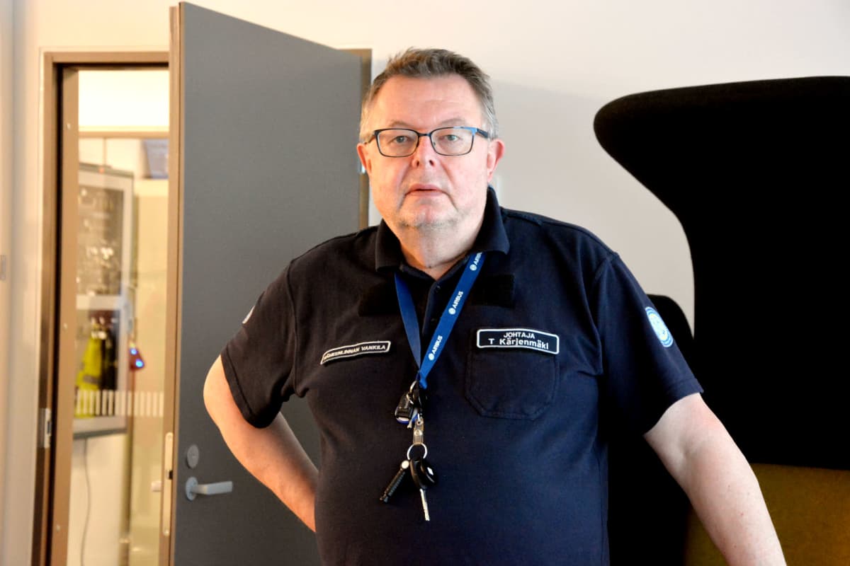 en man i mörk skjorta, nyckelknippa runt halsen och svarta glasögon står inomhus