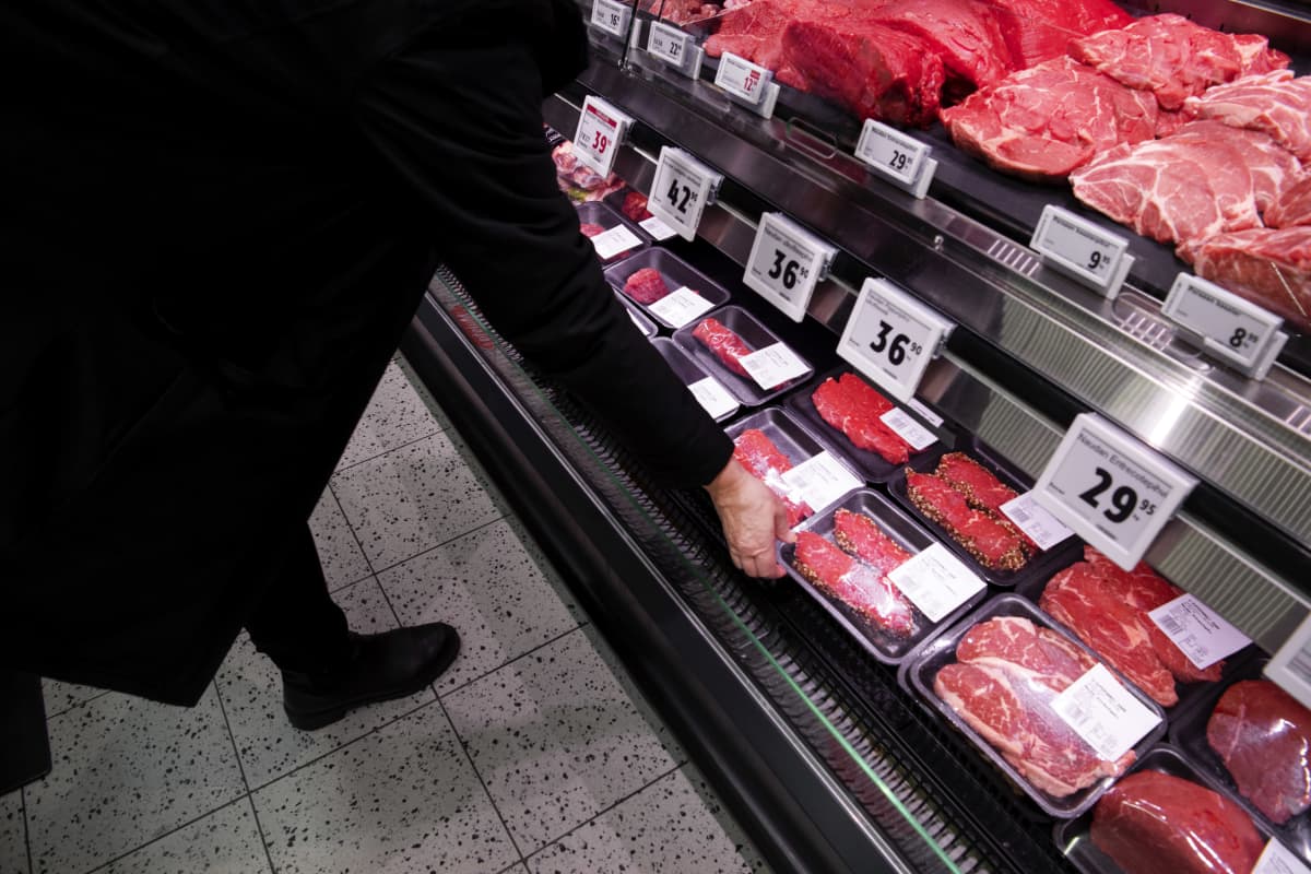 Asiakas ottaa lihapaketin kaupan kylmähyllystä.