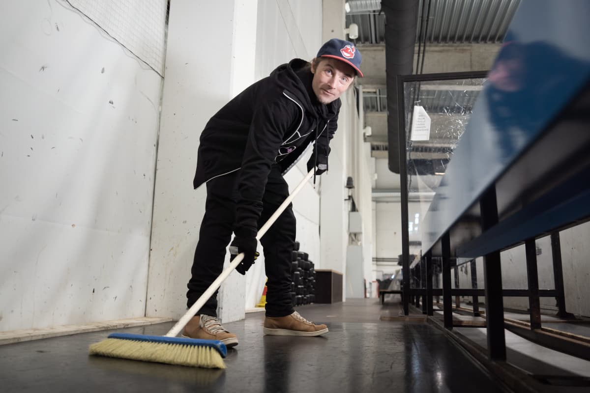 Yhdyskuntapalvelukseen tuomittu Juhani Saunio poseeraa jäähallilla jääkiekkoasennossa harjan kanssa.