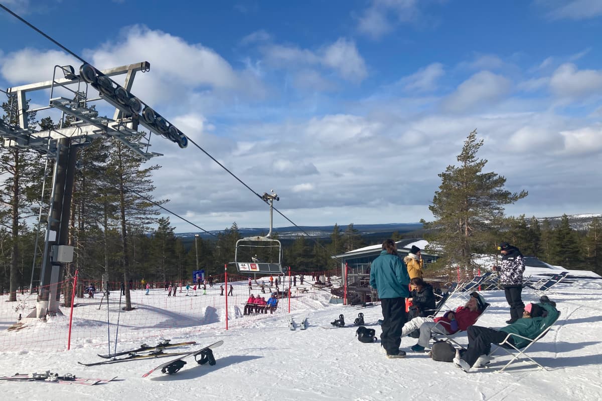 Lasketteluasuisia ihmisiä lekottelee lepotuoleissa hiihtohissin vieressä lumella Ylläksen laskettelukeskuksessa.