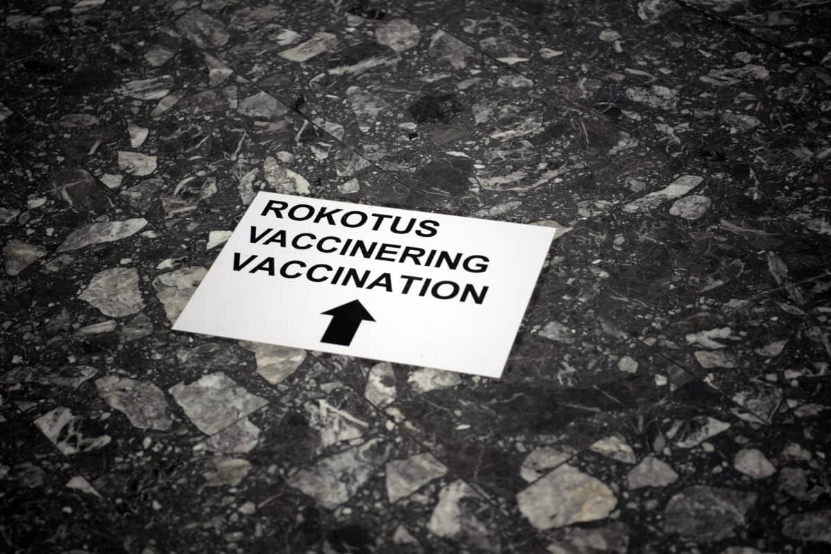 Lattialle kiinnitetty nuolella varustettu opastarra näyttää suunnan kohti rokotuspaikkaa.