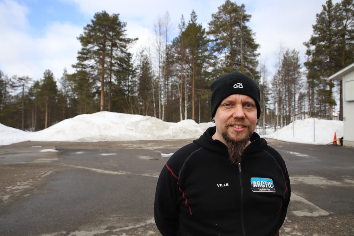 Ville Häkkinen seisoo parkkipaikalla musta takki ja musta pipo päässään.