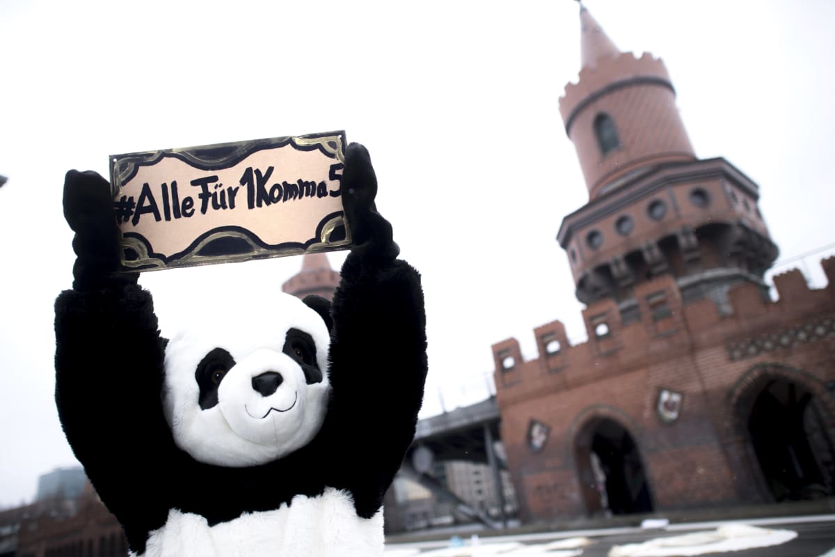 Panda-asuun pukeutunut ihminen pitelee kylttiä jossa lukee saksaksi "Kaikki 1,5:n puolesta"