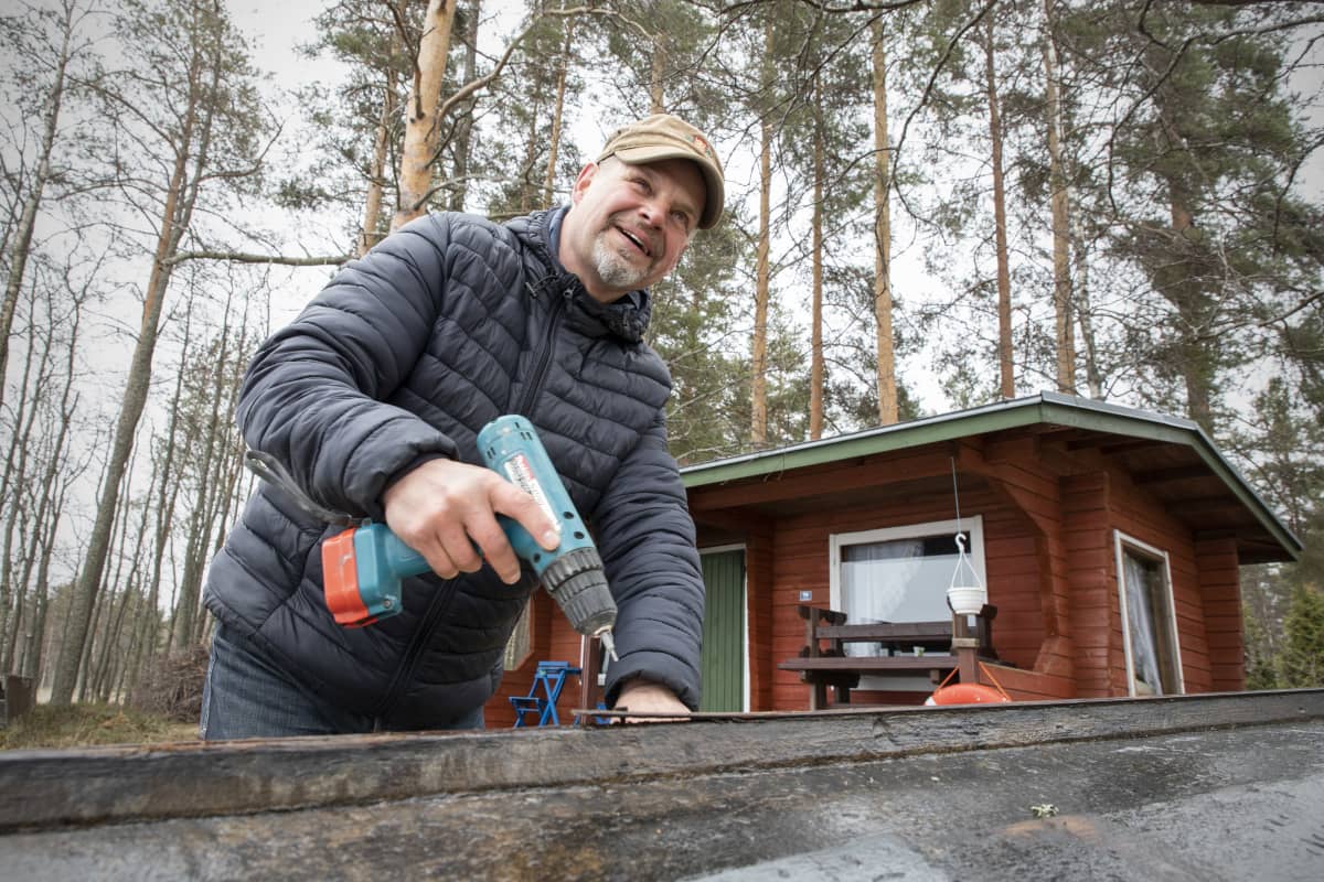 Hymyilevä Kari Kulmala korjaa puuvenettään rantasaunan luona.