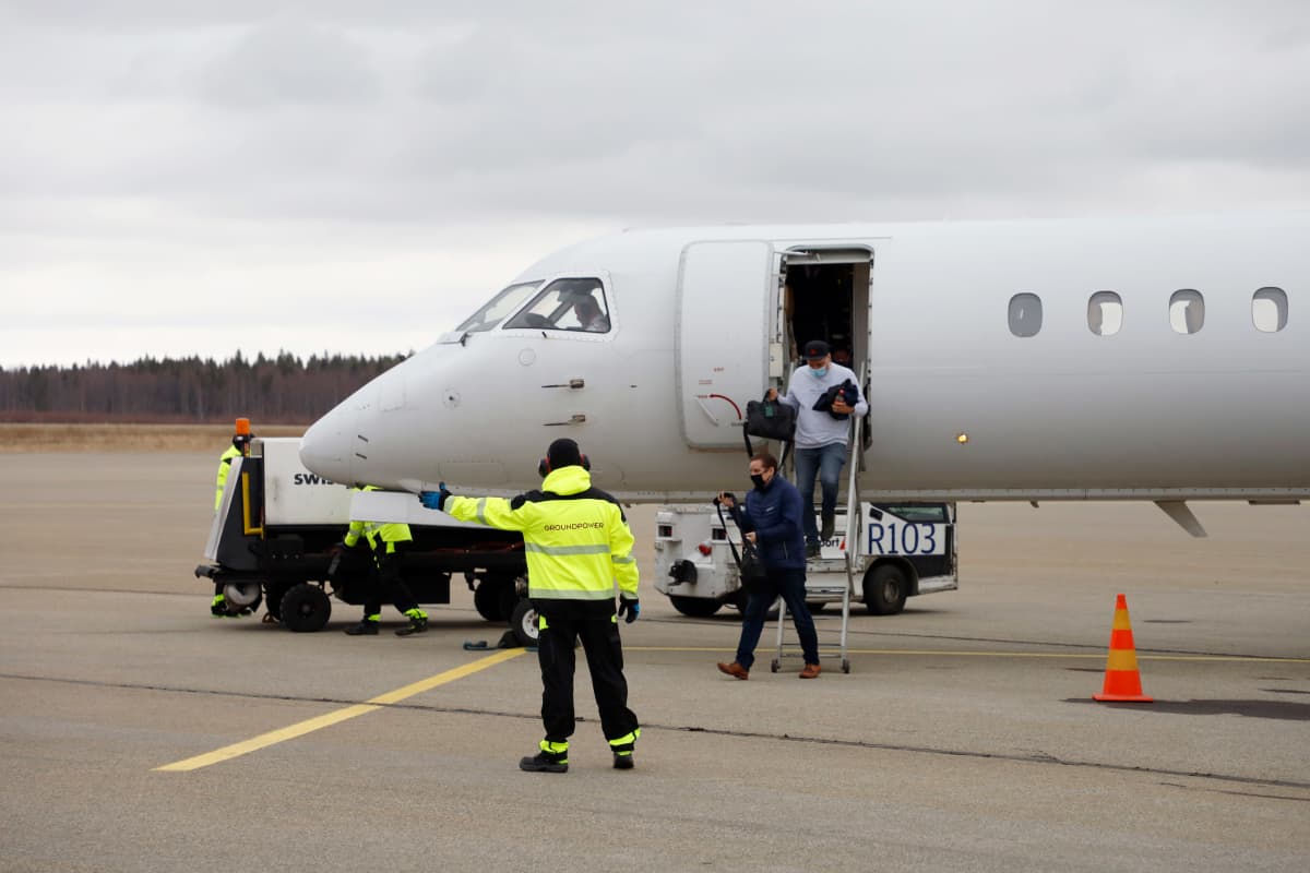 Keltatakkinen maapalveluhenkilökunnan edustaja viittoo Kemi-Tornio lentokentällä, taustalla matkustajakone, josta laskeutuu matkustajia.