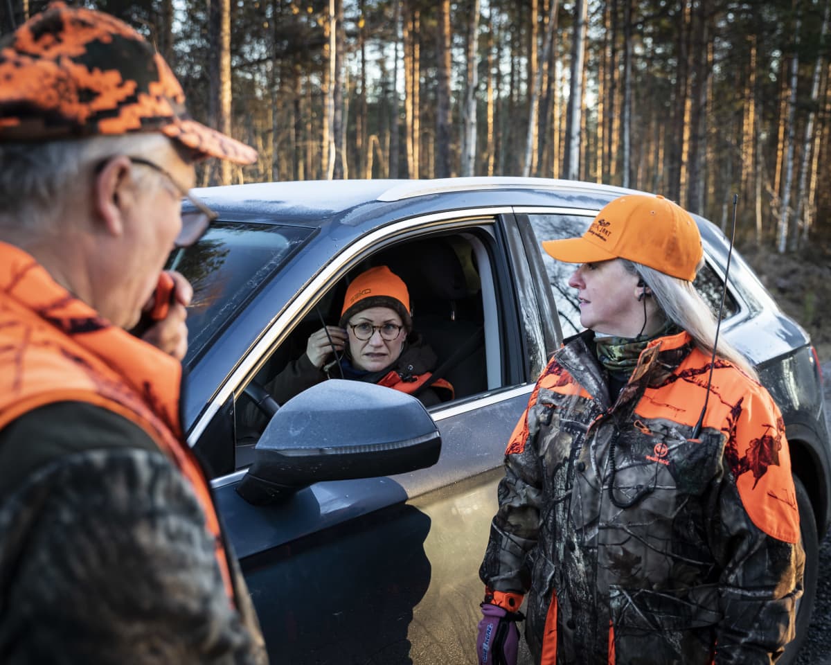 Hirvenmetsästäjiä keskustelemassa. Yksi istuu autossa.