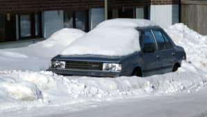 Kuvassa lumeen hautautunut auto kadun varrella.