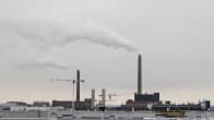 Helein Salmisaaren voimalaitosten yläosat ja piiput, jokta tupruttavat savua ilmaan. Kuvan alaosassa alueen rakennusten kattoja.