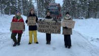 Neljä mielenosoittajaa seisoo lumisella metsätiellä estäen takanaan olevan tukkirekan kulun.