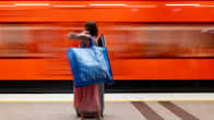 Henkilö nostaa suuren, sinisen kassin olalleen metron kulkiessa hänen edessään.