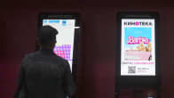 Mies osatamassa lippua elokuvaan, barbie-mainos toisessa automaatissa