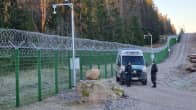 A stretch of fencing along Finland's border with Russia, featuring two officers standing in front of a Border Guard van next to the fence.