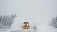 Snowplow clearing a snowy road with a line of vehicles in the background.