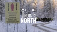 All Points North episode picture showing a sign at the border with Russia and a group of people in the distance. 