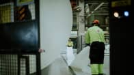 Kaksi työntekijää käsittelemässä suurta paperirullaa tehtaalla.
