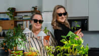 Kaksi naista sisätilassa aurinkolasit silmillään viherkasvien ja kasvivalolamppujen ääressä.