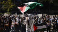 Mielenosoittajia kyltteineen. Joukon edessä seisova ihminen heiluttaa palestiinalaislippua.