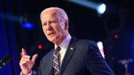 Yhdysvaltain presidentti Joe Biden pitää puhetta tummassa puvussa korokkeen takana, taustalla valonheitin.