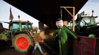 Emmanuel Macronia esittävään naamariin pukeutunut mielenosoittaja traktoreiden vierustalla.