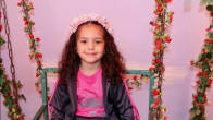 6-vuotias tyttö katsoo kameraan hymyille. Takana on pinkki seinä ja kukkakoristeita.