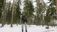 Varusmies seisoo aseen kanssa taisteluvarusteissa keskellä lumista metsää.
