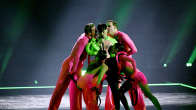 Käärijä vihreässä polerossa lavalla neljän pinkkiin pukeutuneen tanssijan ympäröimänä, jotka ovat nuolevinaan Käärijää.