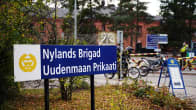 En skylt där det står Nylands brigad på svenska och finska. I bakgrunden syns porten till garnisonsområdet.
