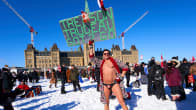 En demonstrant i badbyxor står i snön framför Kanadas parlament. Han bär ett plakat som anklagar Kanadas premiärminister för landsförräderi.