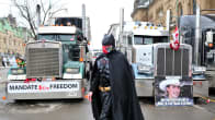 Batman-asuinen mielenosoittaja seisoo kahden ison rekan edessä.