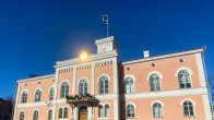 Vaaleanpunainen Loviisan kaupungintalo. Aurinko heijastuu kaupungin vaakunassa korkealla sisäänkäynnin yläpuolella.