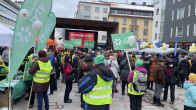 Ihmisiä seisoo vihreiden lippujen ja kylttien kanssa rotuaarian aukolla lavan edessä Oulussa. 