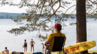 A lifeguard sits in a chair with people standing and sitting on the beach in the background at Tuomiojärvi beach in Jyväskylä. 