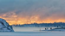 Ihmiset ihailemassa auringonlaskua ja merisumua Helsingissä.