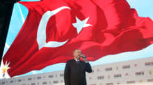 Turkin presidentti Recep Tayyip Erdogan puhuu mikrofoniin, hänen yläpuolellaan liehuu maan lippu.