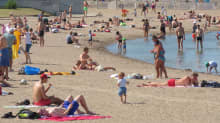 Paljon uima-asuisia ihmisiä hiekkarannalla ja rantavedessä. 