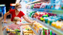 Nainen ja lapsi ruokakaupassa. Lapsi istuu ostoskärryissä. Molemmilla on hengityssuojain. 