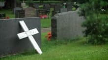 Huonokuntoinen risti nojaa hautakiveen hautausmaalla